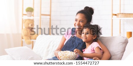 Watching tv together. African american sisters enjoying cartoon with popcorn at home, panorama with empty space