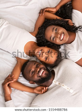 Closeup portrait of cute little african girl and her parents lying on bed and smiling, relaxing at home, top view