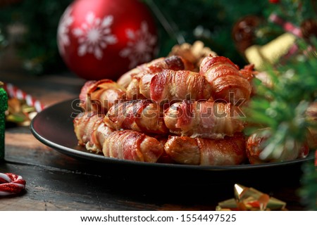 Christmas Pigs in blankets, sausages wrapped in bacon with decoration, gifts, green tree branch on wooden rustic table Royalty-Free Stock Photo #1554497525