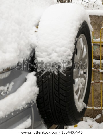 The car is covered with snow in the winter. Spare wheel of a car in the snow. The cold season.