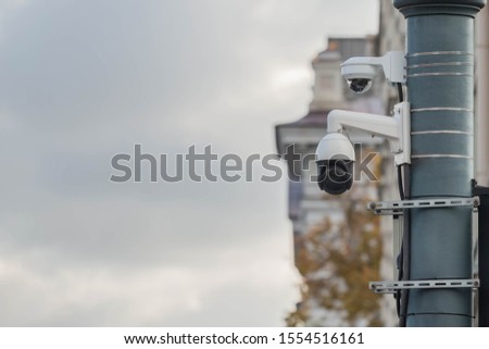 View of a contemporary surveillance CCTV cam attached to metal pole. 360 degrees security video camera in city street on classic building in town background, cloudy sky for copy space