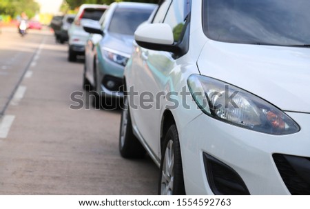 Closeup of front side of white car with  other cars parking in outdoor parking area beside the street in sunny day. The mean of simply transportation in modern world.