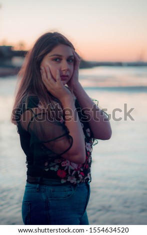 young latina teen with her hands on her face at the beach sunset