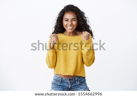 Yes deal mine. Successful african-american cute woman in yellow sweater, smiling happily, celebrating amazing news, making fist pump reacting lucky excellent opportunity, standing white background