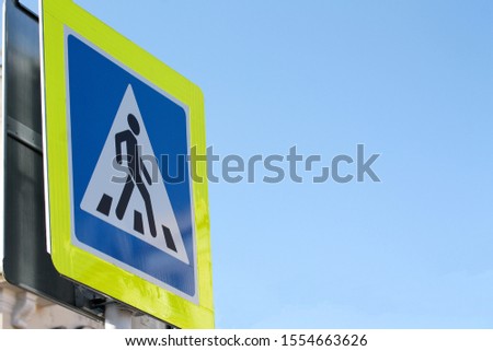 Pedestrian crossing blue sign with yellow light-reflecting frame. Blue sky background with copy space for text. Picture of person crossing the road. Road laws and highway regulations