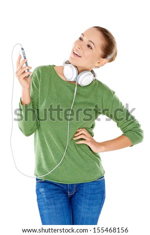 Casual attractive young woman enjoying her music standing with a storage device in her hand and headphones around her neck smiling with pleasure