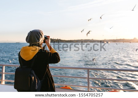Tourist woman taking travel picture with camera of Bosphorus Strait during autumn holidays. View from the back.