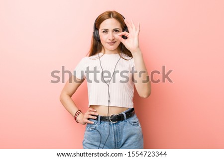 Young caucasian woman listen to music cheerful and confident showing ok gesture.