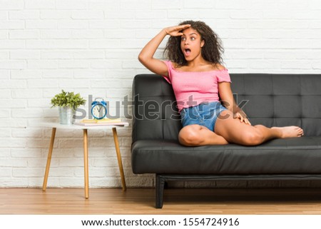 Young african american woman sitting on the sofa looking far away keeping hand on forehead.