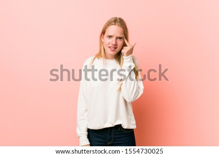 Young blonde teenager woman showing a disappointment gesture with forefinger.