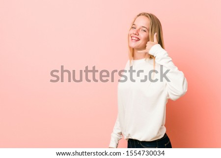 Young blonde teenager woman showing a mobile phone call gesture with fingers.