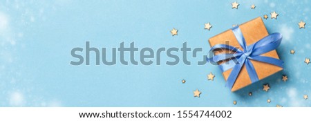 Gift box with blue ribbon on a blue background with decorative stars. Gift concept for a loved one, holiday. Banner .Flat lay, top view