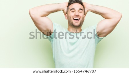 Young handsome man against a green background laughs joyfully keeping hands on head. Happiness concept.