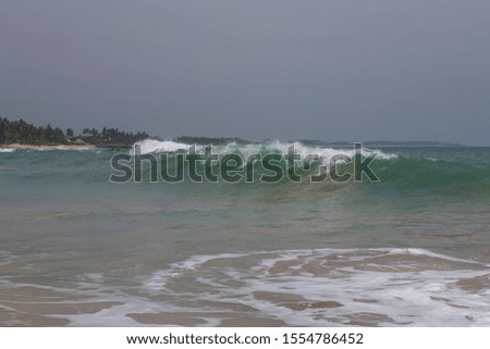 natural copy space shot of a huge wave crushing on the smooth yellow sand beach surface, forming white foam, with the blue sky on the horizon. Tangalle  Sri Lanka