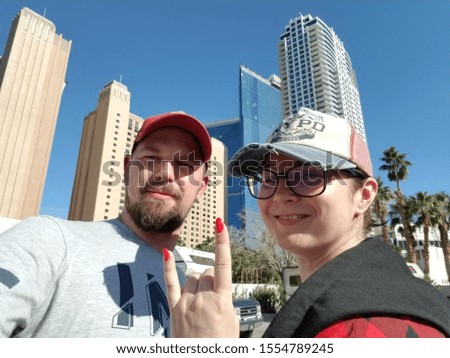 A guy with a girl are standing in baseball caps against the background of skyscrapers. The girl is smiling. Guy wears a beard