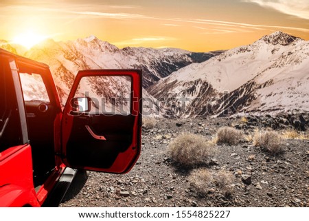 Winter red car on the road. Landscape of mountain peaks full of snow and sunset. Beautiful orange sky and Christmas time. Copy space.Winter road.