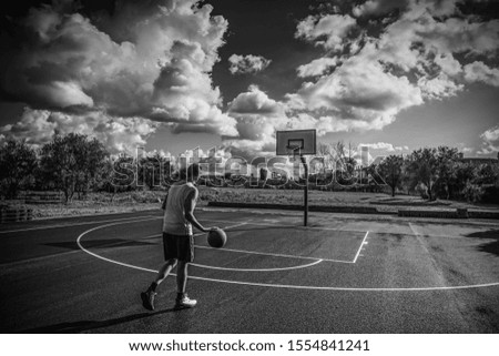 Basketball player dribbling in a playground on a cloudy day. Black and white effect