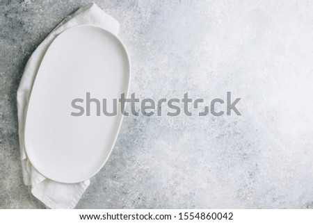 Empty white oval plate and white napkin on light gray background table. Top view. Copy space. Flat lay. Minimal concept