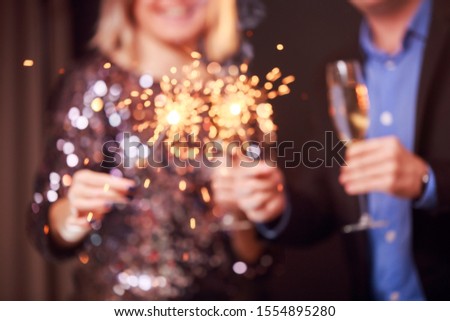 Photo of happy couple with champagne glasses and sparklers on black background