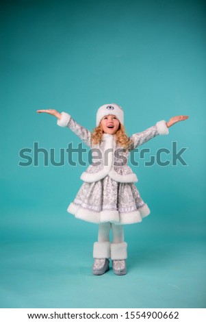 little blonde girl smiling in snow maiden costume isolate on blue background, baby catches snowflakes