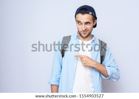 Doubting guy points his finger to the side, portrait, grey background, copy space