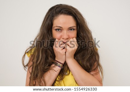 Anxiety - a conceptual image of a beautiful young caucasian woman covering her mouth with her hands and standing outdoors. Scared from something or someone bitting nails.