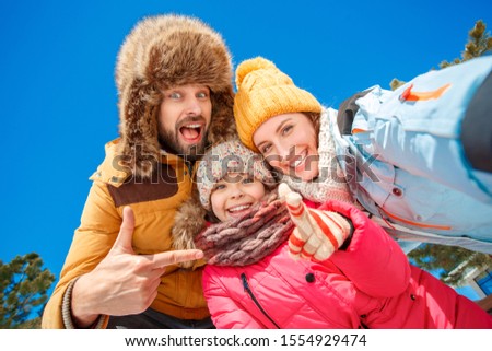 Family on a winter vacation spending time together outdoors taking selfie photo showing thumbs up smiling toothy bottom view
