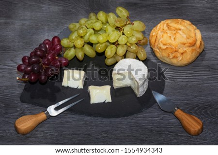 A cheese platter set with somerset goats' cheese, small sprig of grapes and bread on a dark wood background
