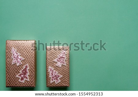 Two gift boxes with small decorative Christmas trees on a green background. Happy New Year and Merry Christmas!

