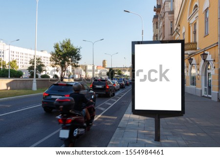 Vertical billboard on the right side of the road on the sidewalk.