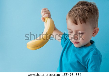 Little Boy Holding and eating an Banana on blue background, food, diet and healthy eating concept.