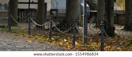 Old black iron poles and chains surrounded by autumn leaves, blurred background