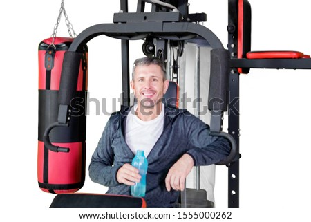 Picture of smiling man holding a bottle of water while taking a break on a gym machine, isolated on white background
