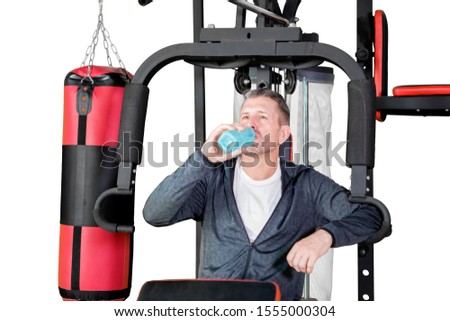 Picture of young man drinking water while resting on a fitness machine, isolated on white background