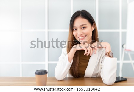 attractive asian officer relax in office, she rest chin on her hand, she drinking hot coffee, she feeling happy and smile, happiness organization