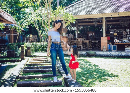Indonesian young beautiful mother in casual clothes walking with  little cute daughter in dress outdoors on background of terrace
