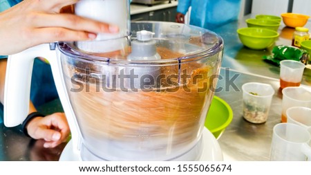 Electric food processor in fast spinning action while mixing a variety of ingredients together. The process renders the mixing bowl sample contents blurry. Royalty-Free Stock Photo #1555065674
