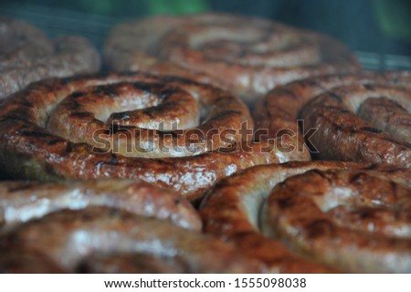 Boerewors sausages sizzling on a charcoal barbecue grill. Boerewors is a typical South African sausage made from minced beef, but it can also be made with minced pork, lamb or both.  Royalty-Free Stock Photo #1555098038