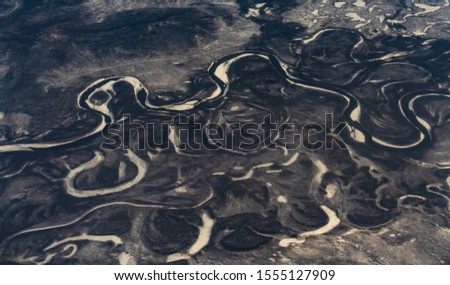 The view from the height of the riverbed. View from the plane to the valley. A river meanders in a vast plain. There is snow on the banks. Dark and violet shades prevail