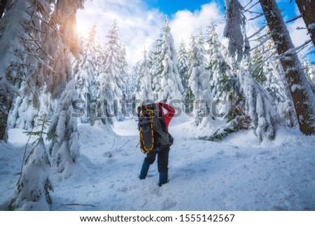 Travel photographer with backpack and the camera take a picture of winter forest.