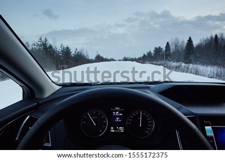 Driving a car in the winter in dangerous road conditions. View through the windshield of the car on the road in the evening. The hands of the driver on the steering wheel and the speedometer control.
