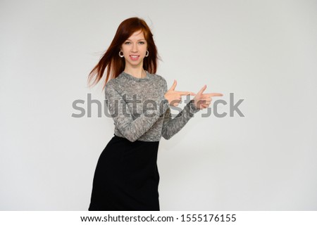 Portrait of a pretty woman, red-haired student girl with long straight hair on a white background in a gray dress. Talking to the camera, showing emotions, smiling.