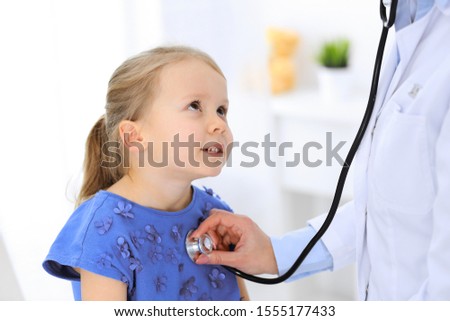 Doctor examining a little girl by stethoscope. Happy smiling child patient at usual medical inspection. Medicine and healthcare concepts
