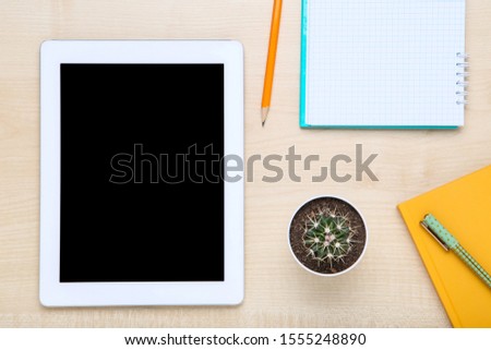 Tablet computer with notepads and cactus on brown wooden table