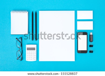 Set of variety blank office objects organized for company presentation or corporate identity. Isolated on blue paper background. Top view.