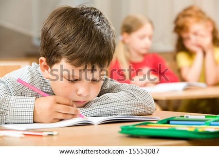 Portrait of bored pupil putting his head on desk and drawing something in copybook at lesson
