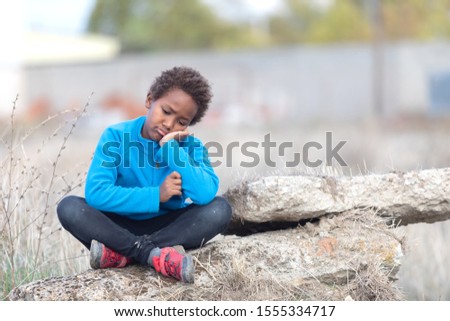 Bored child with blue jersey sitting on a rock in the countryside