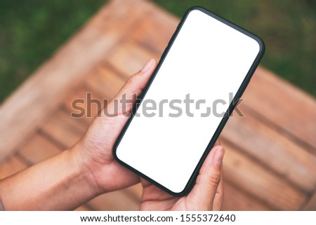 Top view mockup image of hands holding black mobile phone with blank white screen