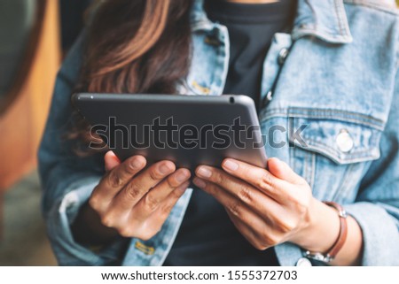 Closeup image of a woman holding and using tablet pc while sitting in cafe