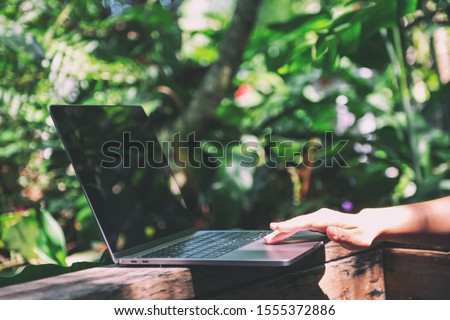 Closeup image of hands working and touching on laptop touchpad on wooden balcony in the garden